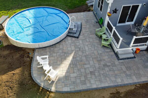 Above ground pool surrounded by landscaping and stone paver patio