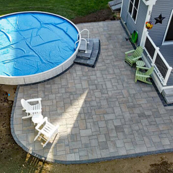 Above ground pool surrounded by landscaping and stone paver patio