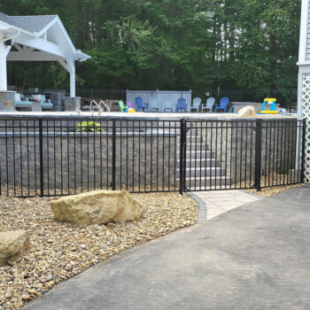 Black fence surrounding raised pool area with stone retaining wall