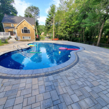 In ground pool surrounded by lush landscaping and stone pavers
