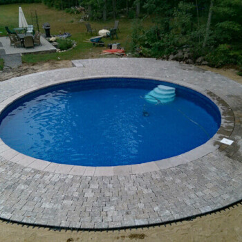 Round in ground pool surrounded by stone pavers